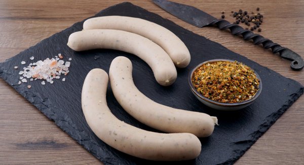 Vier feine Bratwürste angerichtet auf einem Schiefertablett angerichtet mit Gewürzen.