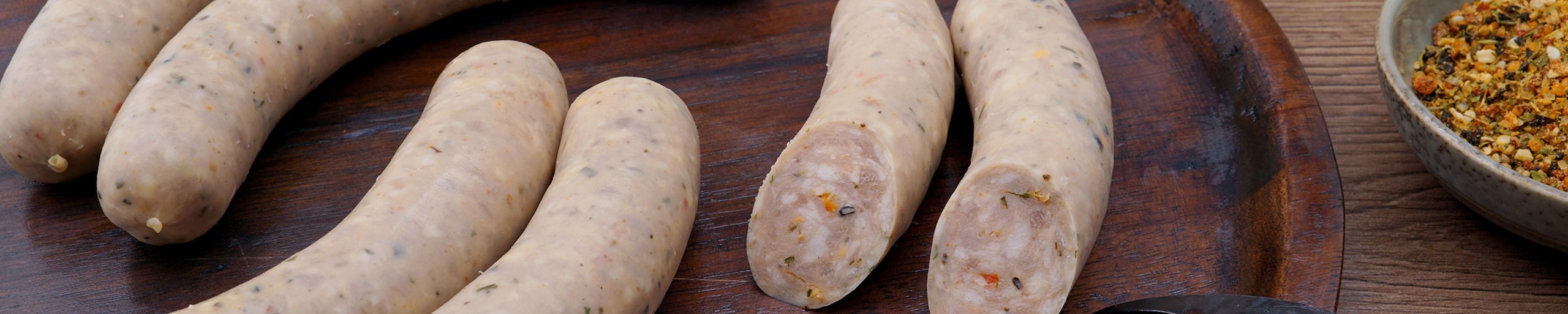 Bildausschnitt von feinen Bratwürsten angerichtet auf einem Holzbrett.
